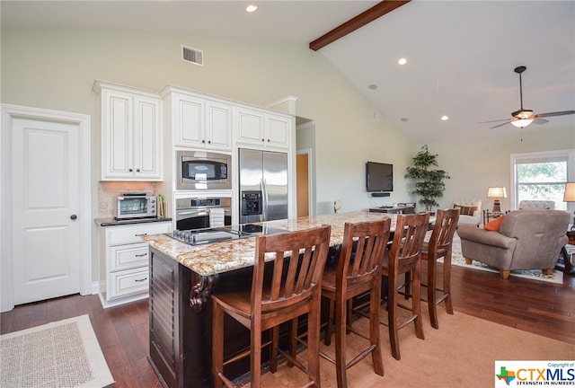 kitchen featuring a kitchen island, built in appliances, dark hardwood / wood-style floors, light stone countertops, and ceiling fan