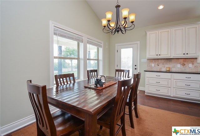 dining space featuring dark wood-type flooring, an inviting chandelier, vaulted ceiling, and plenty of natural light