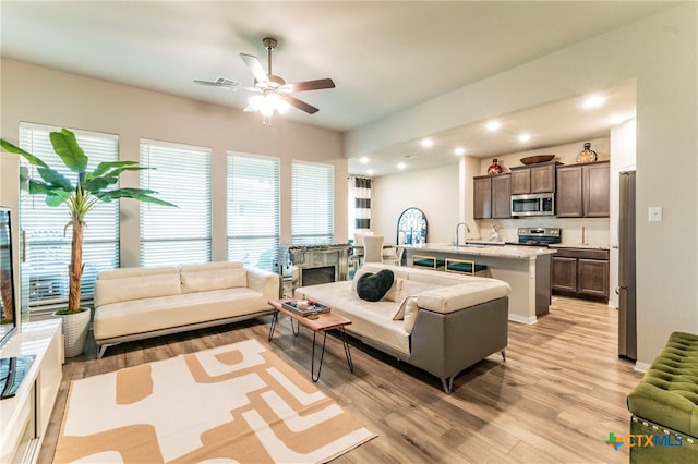 living room with ceiling fan, sink, and light hardwood / wood-style flooring