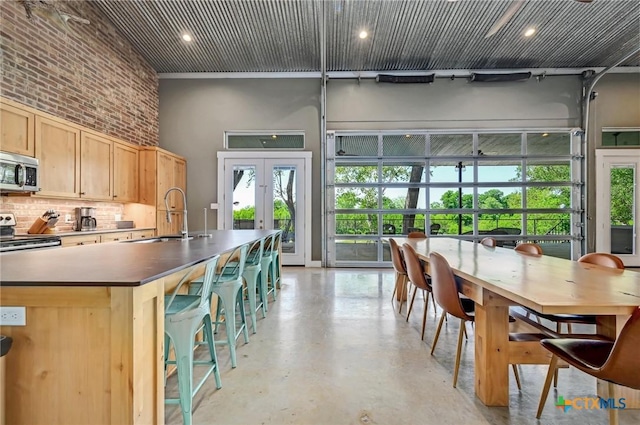 kitchen with a sink, a towering ceiling, finished concrete flooring, backsplash, and appliances with stainless steel finishes