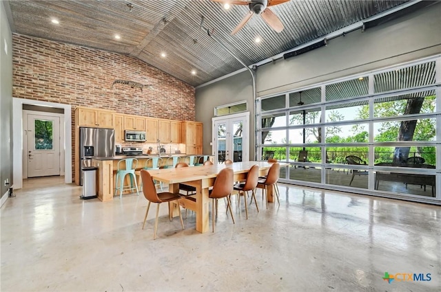 dining room with high vaulted ceiling, brick wall, concrete floors, and ceiling fan