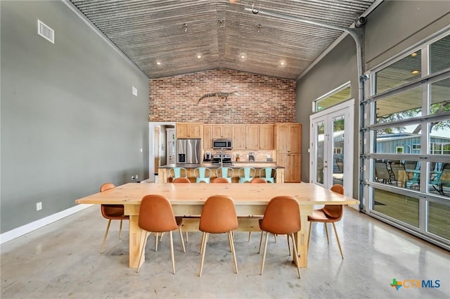 dining space featuring brick wall, french doors, finished concrete floors, and high vaulted ceiling