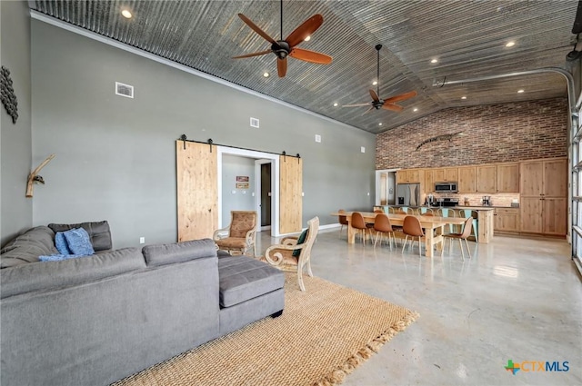 living area with a barn door, visible vents, concrete floors, high vaulted ceiling, and ceiling fan