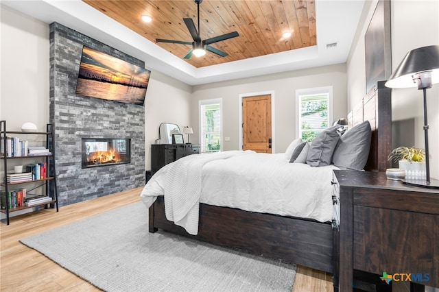 bedroom featuring a fireplace, a raised ceiling, wood ceiling, ceiling fan, and light hardwood / wood-style flooring