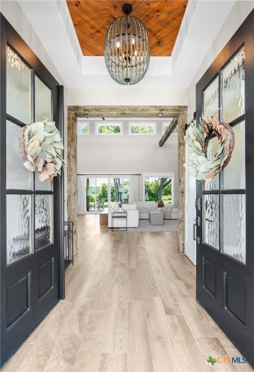 foyer with light hardwood / wood-style floors, a notable chandelier, wooden ceiling, and a raised ceiling