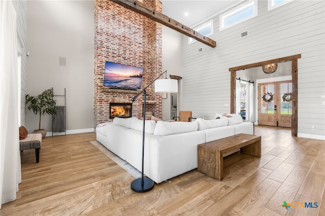 living room featuring a high ceiling, a fireplace, light hardwood / wood-style flooring, and plenty of natural light