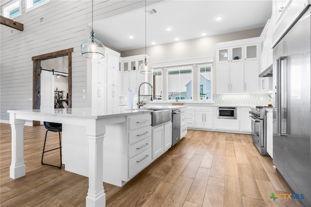 kitchen featuring premium appliances, sink, an island with sink, white cabinetry, and decorative light fixtures