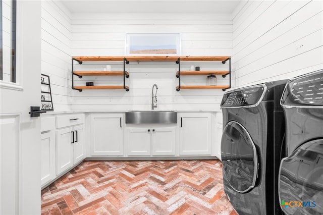 clothes washing area with wood walls, cabinets, sink, and washer and dryer