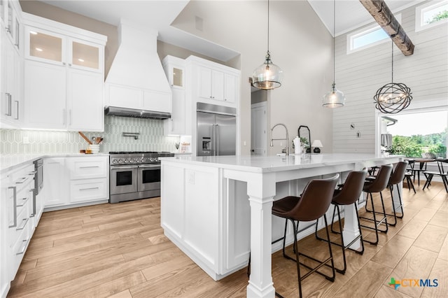 kitchen featuring a center island with sink, white cabinetry, custom range hood, high end appliances, and high vaulted ceiling