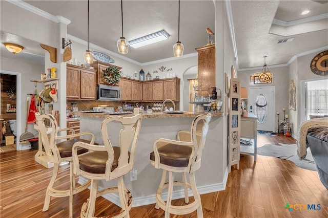 kitchen featuring brown cabinets, stainless steel microwave, decorative light fixtures, light wood-style flooring, and a breakfast bar area