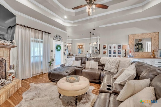 living room featuring ceiling fan, ornamental molding, light wood-style floors, and a raised ceiling