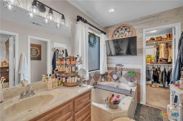 full bath with a walk in closet, a garden tub, vanity, and visible vents