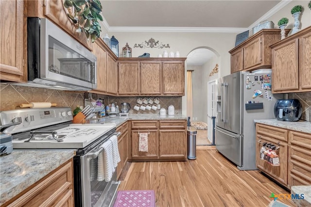 kitchen featuring ornamental molding, arched walkways, appliances with stainless steel finishes, and light wood finished floors