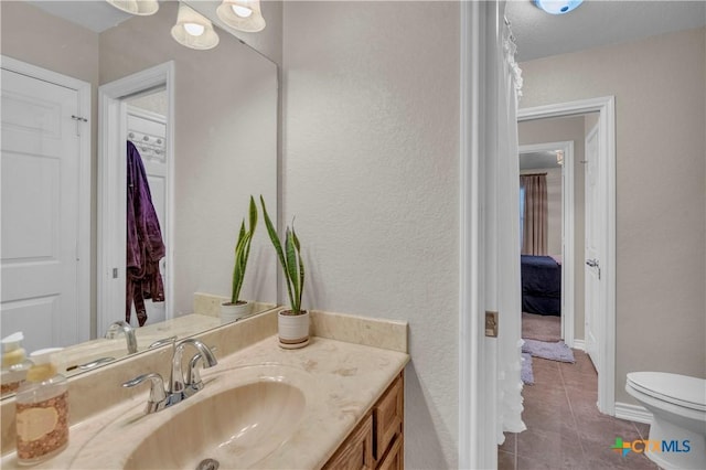 bathroom with toilet, baseboards, tile patterned flooring, a textured wall, and vanity