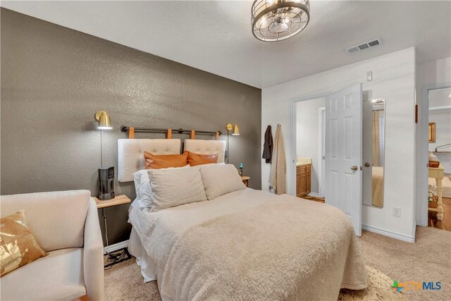 bedroom with baseboards, ensuite bathroom, visible vents, and carpet