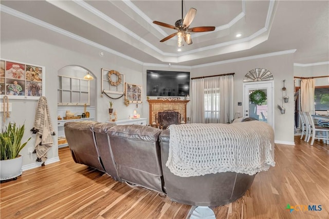 living area featuring ceiling fan, crown molding, light wood finished floors, and a raised ceiling