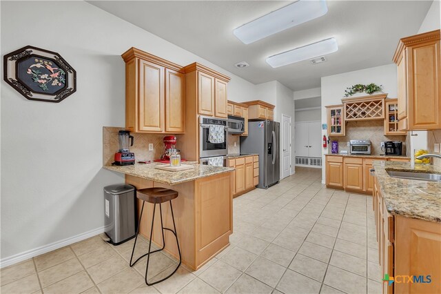 kitchen with sink, tasteful backsplash, a breakfast bar area, light stone countertops, and appliances with stainless steel finishes