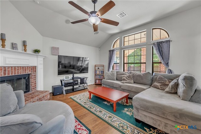 living room featuring a brick fireplace, hardwood / wood-style flooring, ceiling fan, and vaulted ceiling