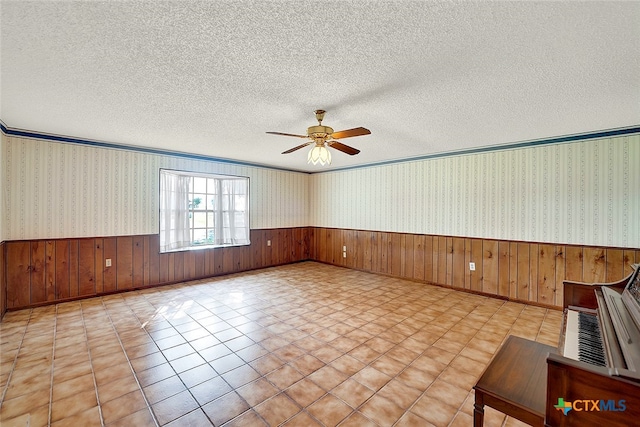 unfurnished room with crown molding, wooden walls, a textured ceiling, and ceiling fan