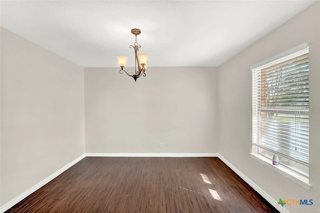 empty room with dark hardwood / wood-style flooring and a chandelier