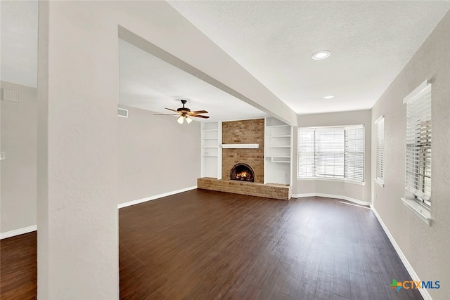 unfurnished living room featuring built in shelves, dark hardwood / wood-style floors, a textured ceiling, ceiling fan, and a brick fireplace