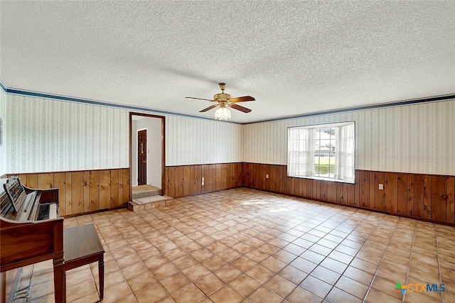 unfurnished living room featuring a textured ceiling, wood walls, and ceiling fan