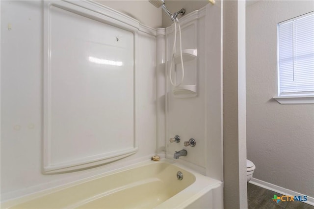 bathroom featuring a textured wall, toilet, washtub / shower combination, wood finished floors, and baseboards