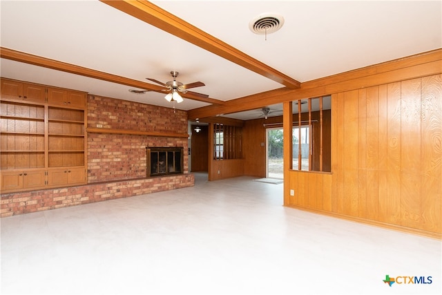 unfurnished living room with a fireplace, wooden walls, ceiling fan, and beam ceiling