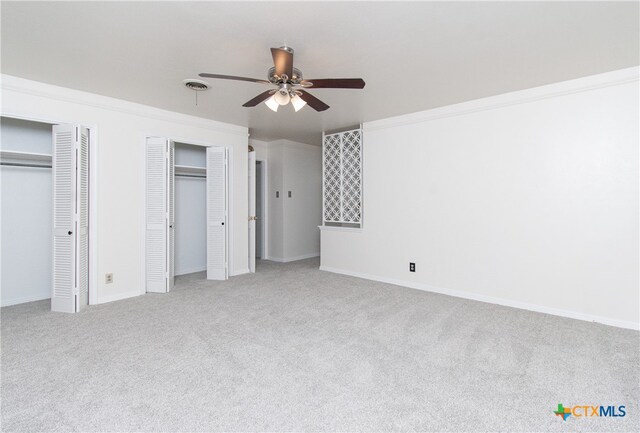 unfurnished bedroom with ceiling fan, multiple closets, and light colored carpet