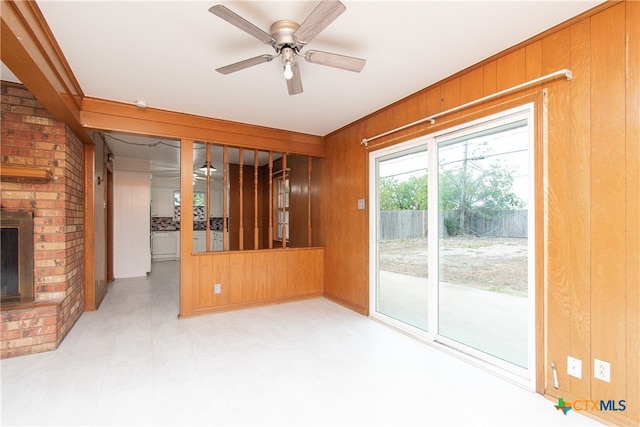 unfurnished living room featuring a brick fireplace, wooden walls, and ceiling fan