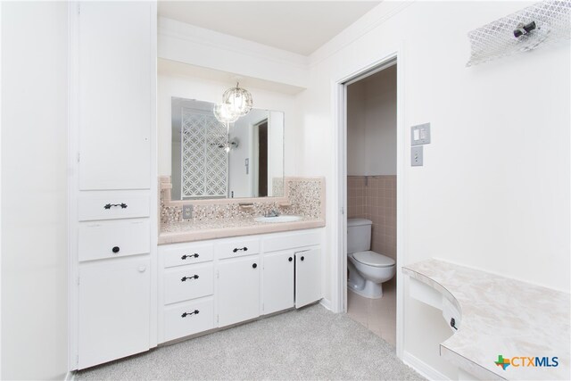 bathroom featuring an inviting chandelier, vanity, crown molding, toilet, and tile walls