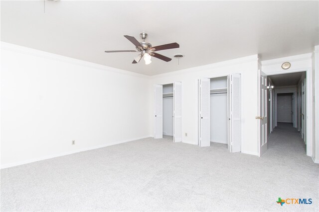 unfurnished bedroom featuring multiple closets, light carpet, ceiling fan, and crown molding