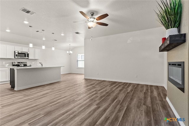 unfurnished living room featuring hardwood / wood-style flooring, lofted ceiling, sink, a textured ceiling, and ceiling fan with notable chandelier