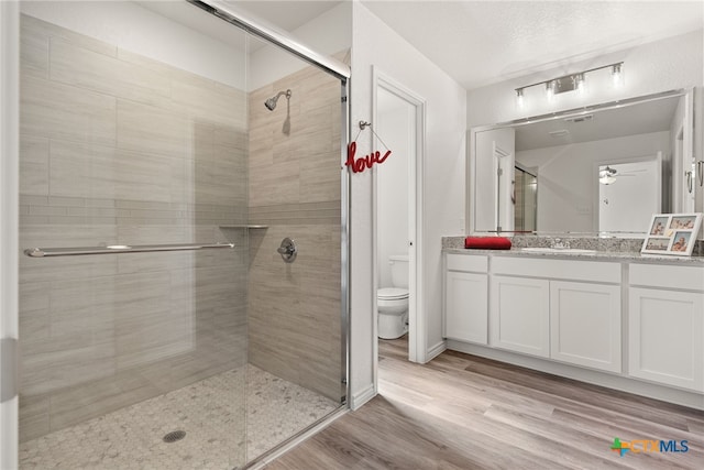 bathroom featuring a shower with door, toilet, ceiling fan, wood-type flooring, and vanity