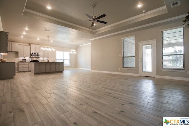 unfurnished living room with ceiling fan with notable chandelier, light hardwood / wood-style flooring, crown molding, and a tray ceiling