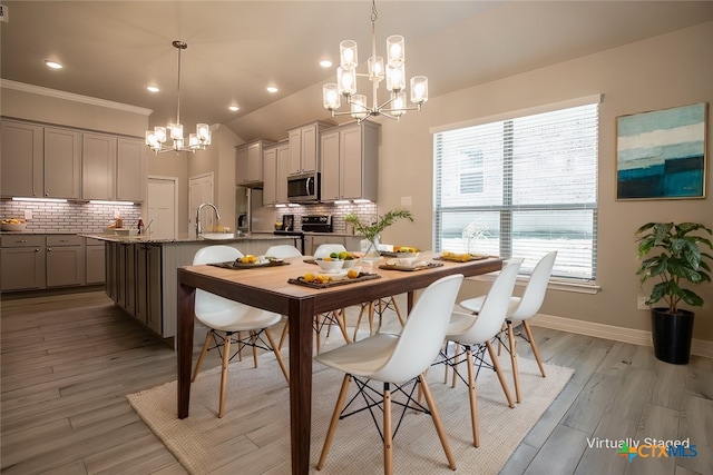 dining area with light wood-type flooring, sink, a notable chandelier, and ornamental molding