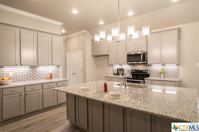 kitchen featuring sink, light stone counters, backsplash, hanging light fixtures, and light wood-type flooring