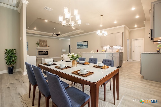 dining room featuring ceiling fan with notable chandelier, light hardwood / wood-style floors, sink, crown molding, and a tray ceiling