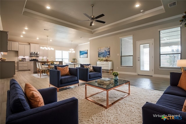 living room featuring light hardwood / wood-style floors, ceiling fan with notable chandelier, ornamental molding, and a tray ceiling