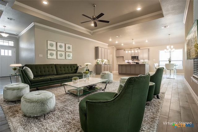 living room with ceiling fan with notable chandelier, a raised ceiling, and ornamental molding