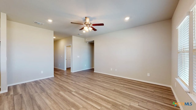 empty room featuring a wealth of natural light, ceiling fan, and light wood-type flooring