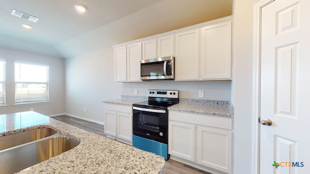 kitchen with stainless steel appliances, white cabinetry, light stone counters, and vaulted ceiling