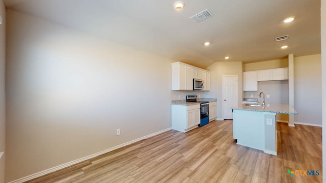 kitchen with stainless steel appliances, an island with sink, light stone countertops, white cabinetry, and light hardwood / wood-style flooring