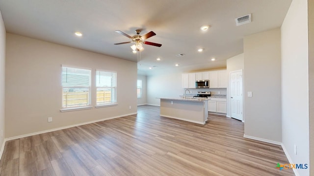 kitchen featuring white cabinets, stainless steel appliances, an island with sink, and light hardwood / wood-style flooring