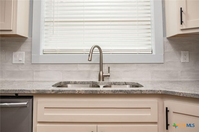 interior details with stainless steel dishwasher, backsplash, light stone counters, and sink