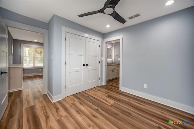 unfurnished bedroom featuring connected bathroom, a closet, light hardwood / wood-style flooring, and ceiling fan