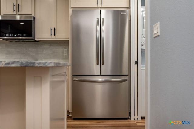 kitchen with decorative backsplash, appliances with stainless steel finishes, light wood-type flooring, and light stone countertops