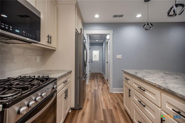 kitchen featuring light stone countertops, appliances with stainless steel finishes, light wood-type flooring, decorative backsplash, and pendant lighting