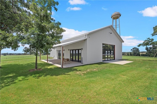 rear view of house featuring a rural view, a lawn, and a patio