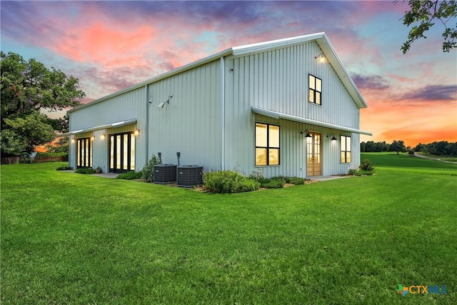 back house at dusk featuring central air condition unit and a lawn